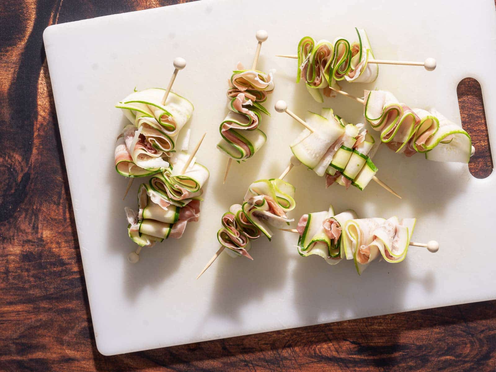 Skewers with rolled zucchini and prosciutto arranged on a white cutting board make the perfect zucchini appetizer.