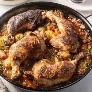A skillet with Cajun-spiced chicken legs resting on a hearty mix of potatoes, carrots, and herbs in a savory sauce.