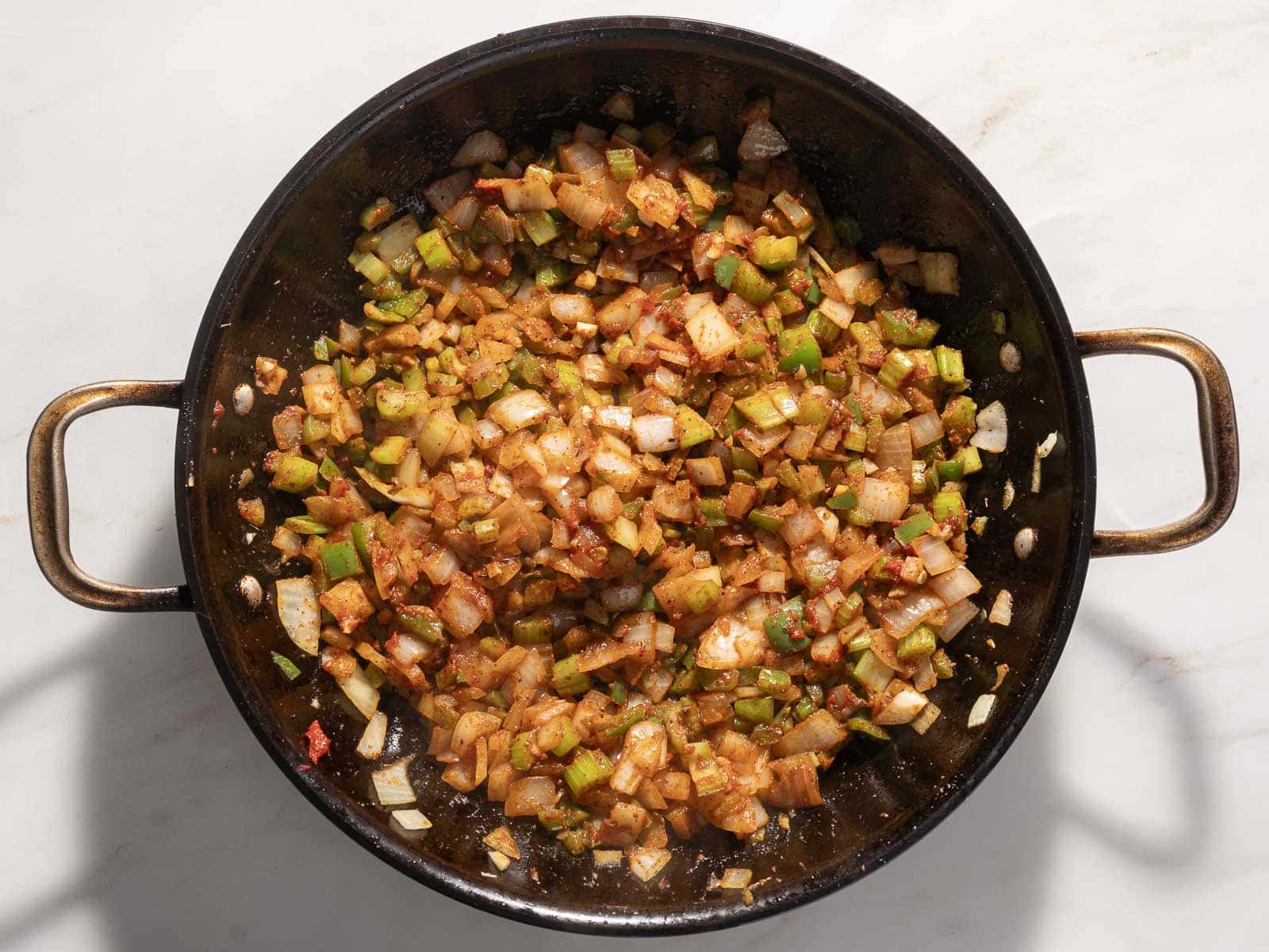A pan filled with saut&eacute;ed vegetables, including chopped onions and green peppers, mixed with spices and chunks of chicken on a stovetop, creating a delightful Cajun-inspired dish.