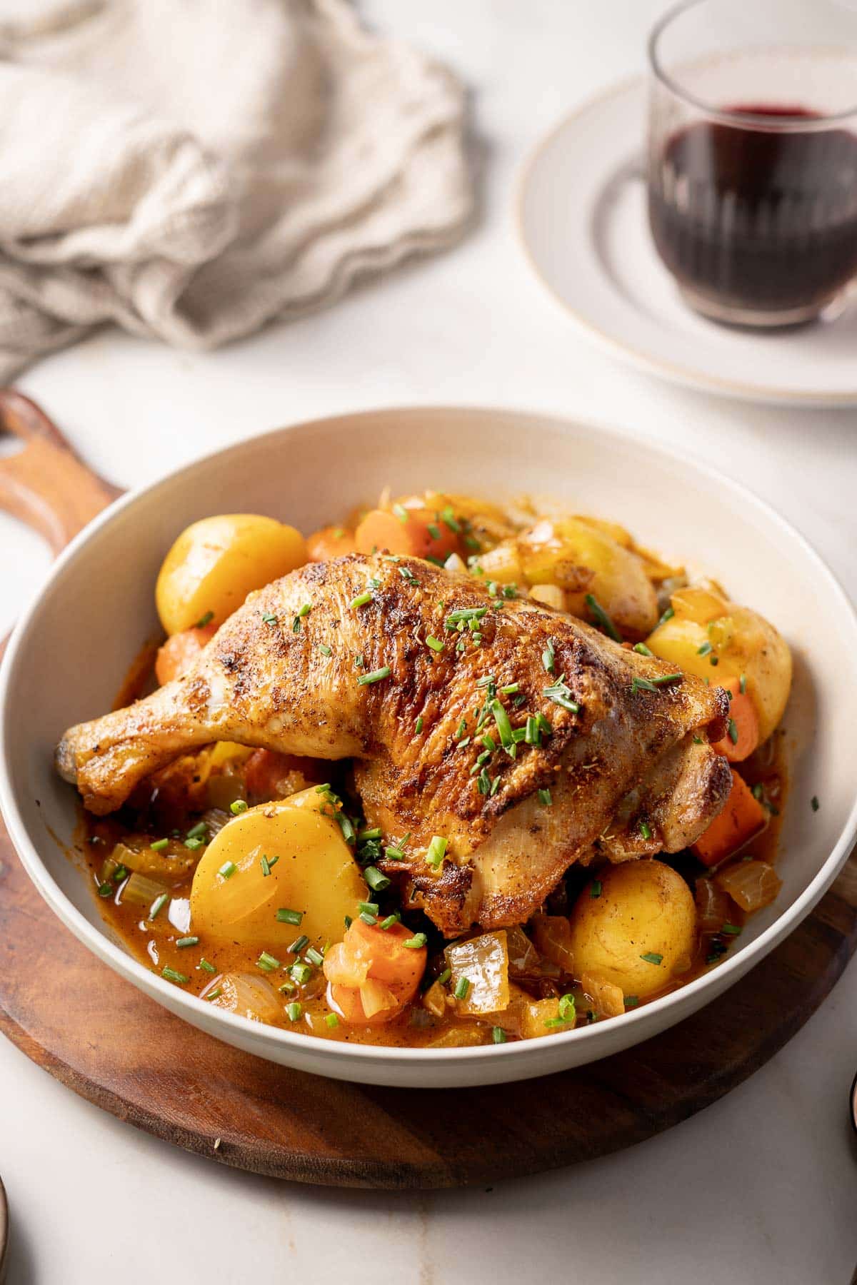 A dish featuring roasted chicken, potatoes, and vegetables garnished with herbs exudes a Cajun flair. A glass of red wine is in the background.