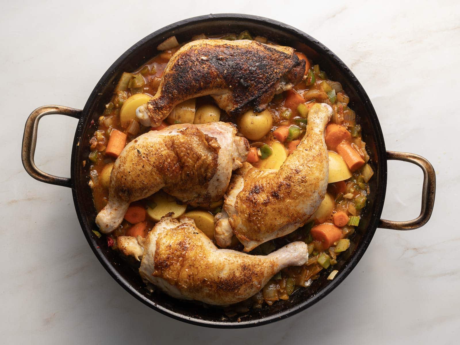 Roasted Cajun chicken pieces in a round pan with carrots, potatoes, and vibrant vegetables on a light background.