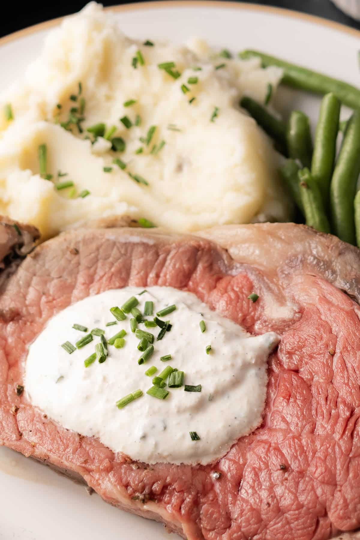 A plate featuring roast beef with velvety horseradish sauce, mashed potatoes topped with chives, and green beans.