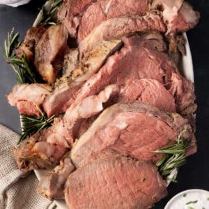 Slices of sous vide prime rib garnished with rosemary on a white platter.