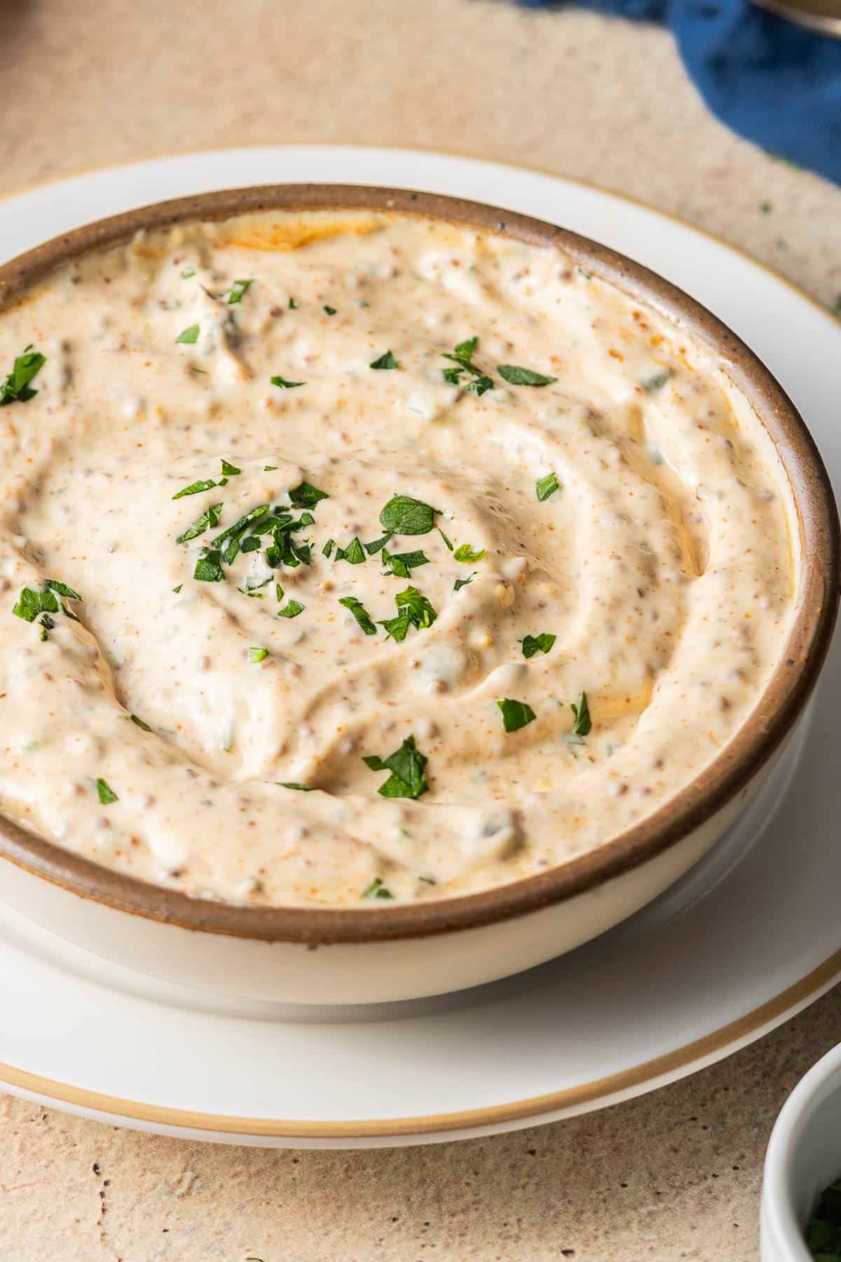A bowl of creamy dip, perfect for any feast, garnished with chopped herbs on a white plate.