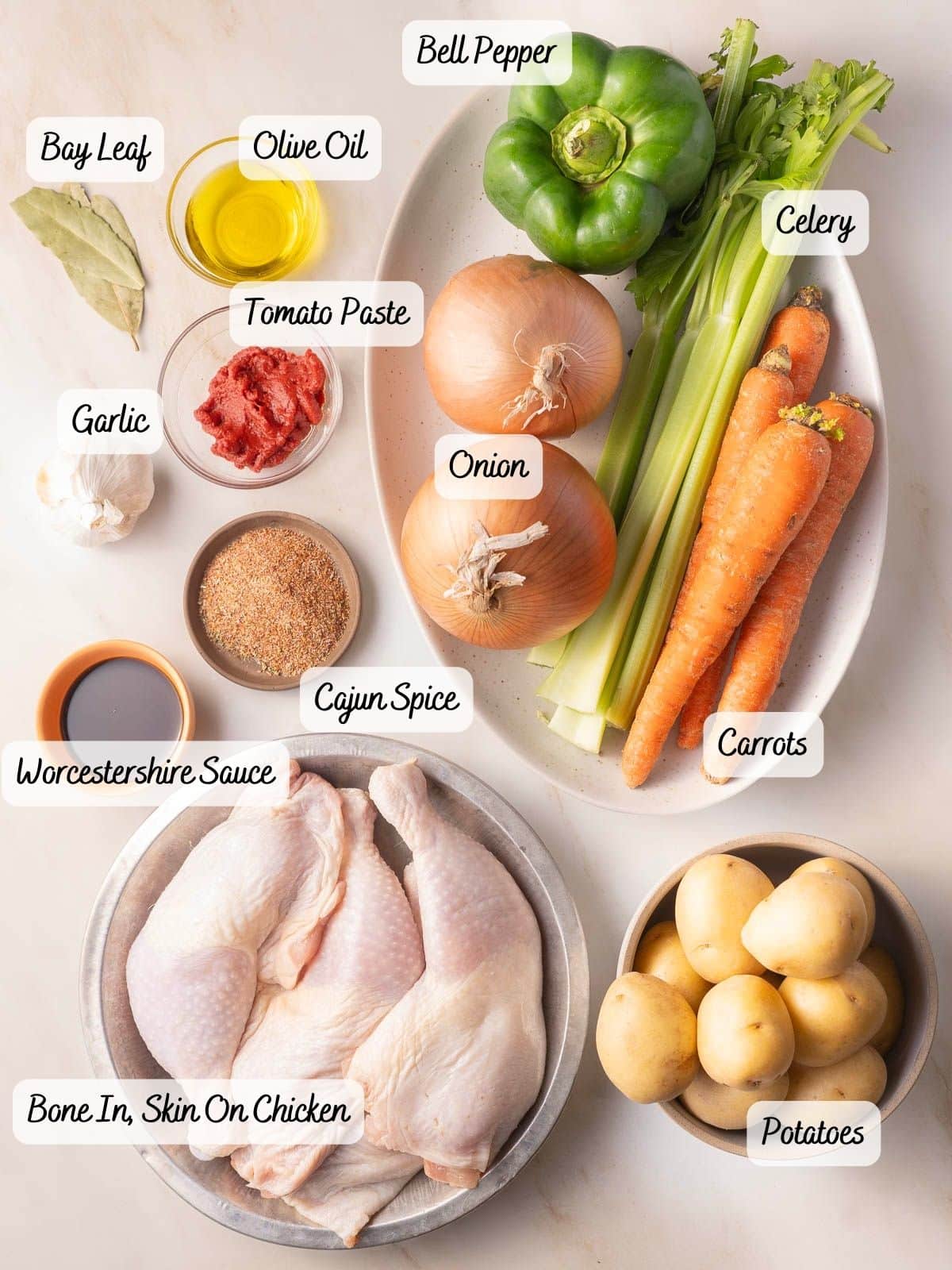 A colorful array of ingredients for a hearty Cajun stew is displayed, featuring succulent chicken, potatoes, olive oil, bay leaf, tomato paste, and garlic. The mix is enhanced with Worcestershire sauce and vibrant vegetables like bell pepper, onion, celery, and carrots.