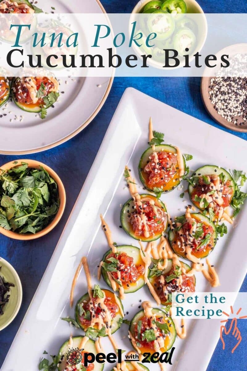 Plates of tuna poke cucumber bites topped with sauce and herbs on a blue surface, surrounded by small bowls of garnishes.