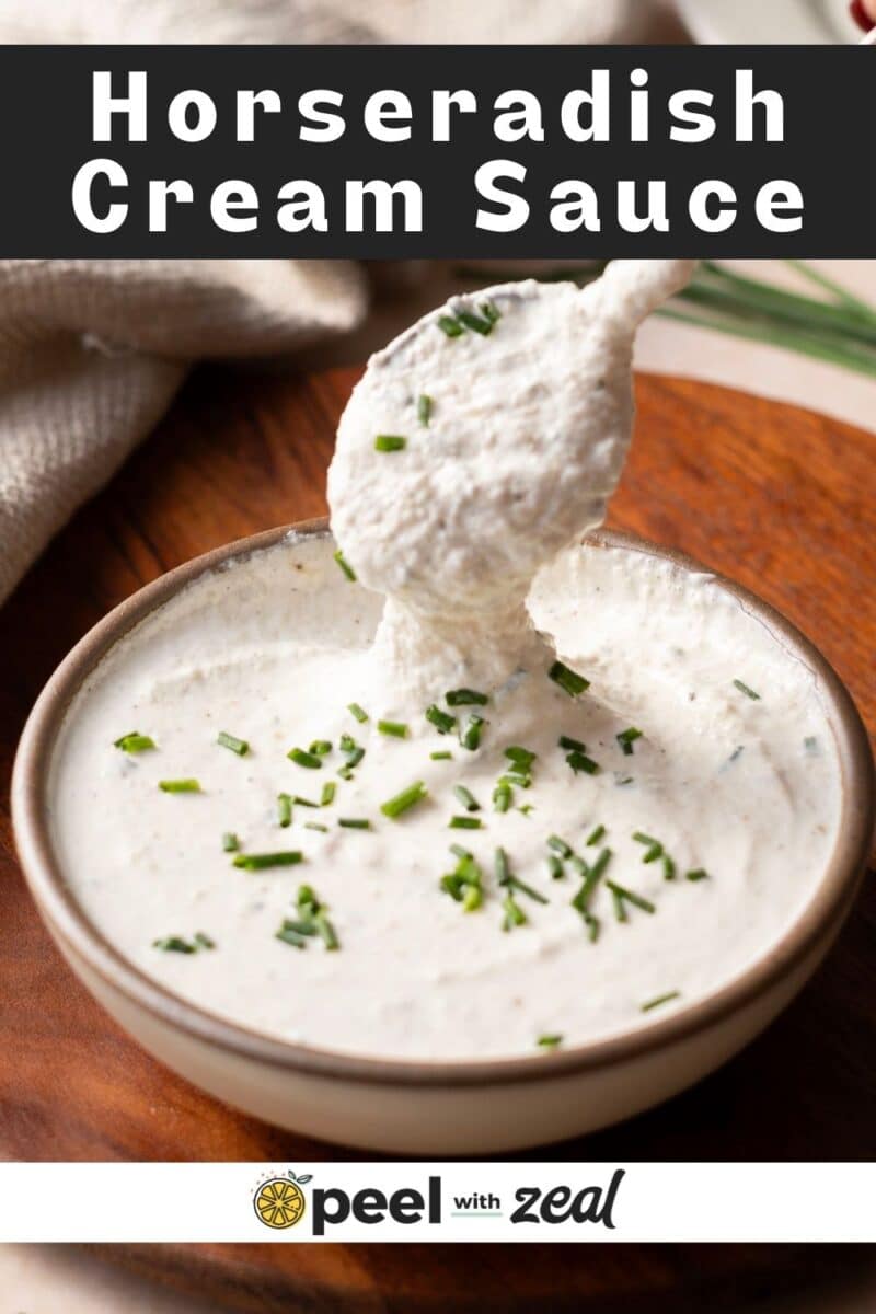 A bowl of creamy horseradish sauce garnished with chopped chives, with a spoon lifting some of the tangy mixture.