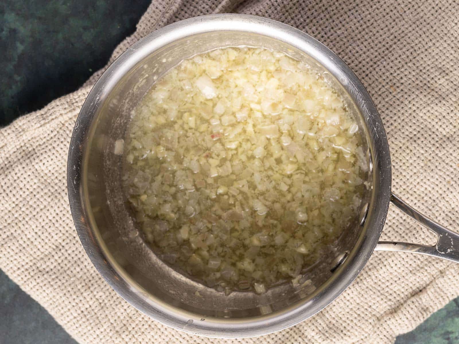 A pot filled with finely chopped onions simmering in a savory au jus rests on a textured beige cloth.