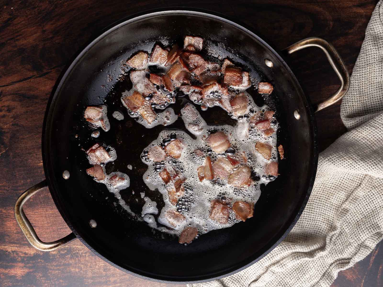 Diced crispy bacon in a cast iron pan.