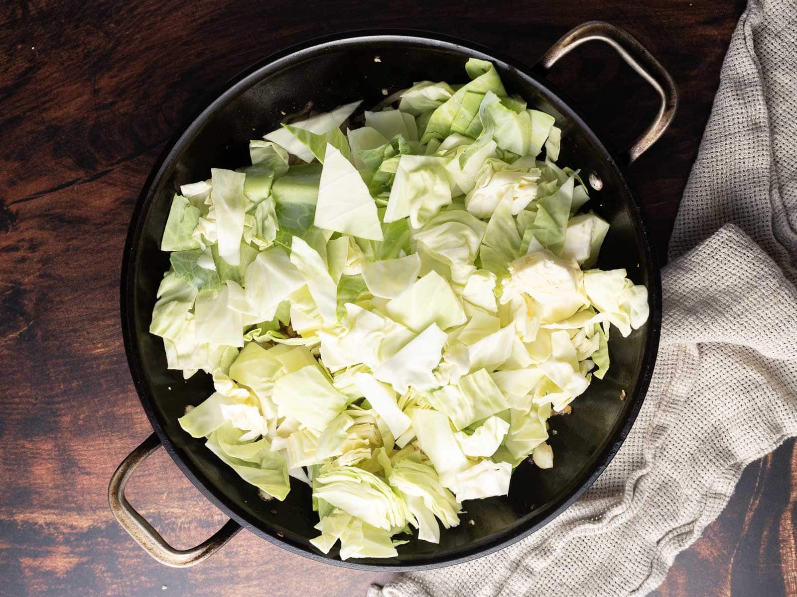 Adding fresh cubes of cabbage to the pan.