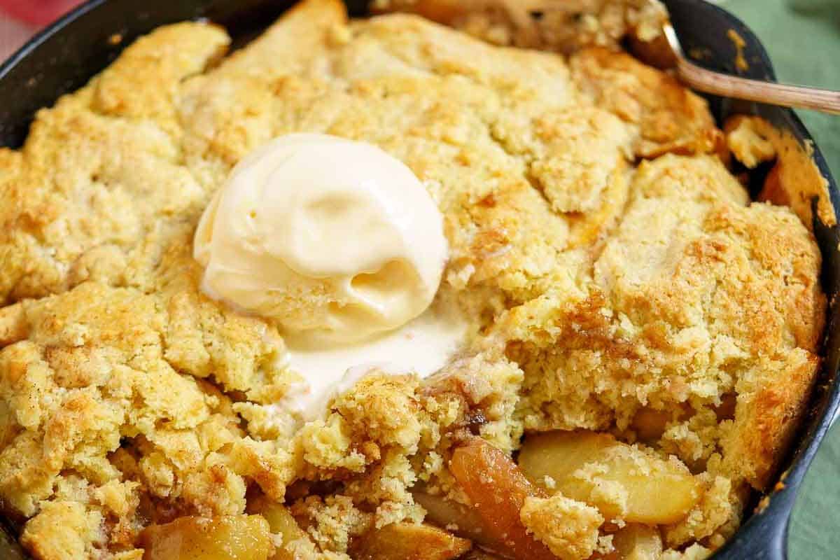 Close-up of a gluten-free baked apple cobbler topped with a scoop of vanilla ice cream in a dark dish, perfect for Thanksgiving.