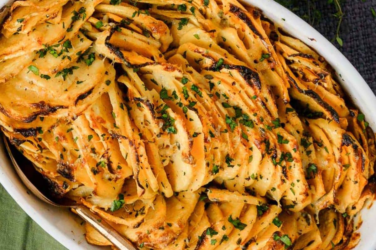 A casserole dish filled with sliced, roasted potatoes topped with chopped parsley makes for a delightful gluten-free addition to your Thanksgiving spread.