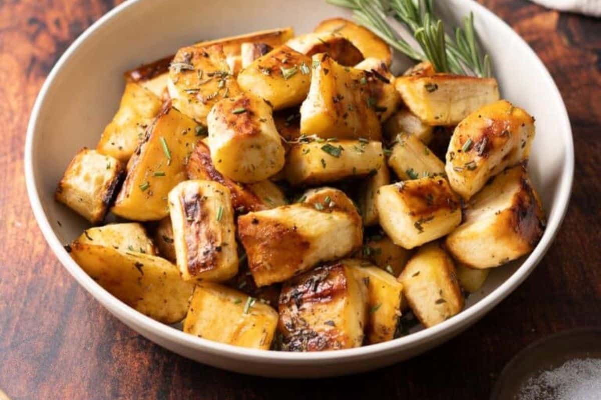 A bowl of roasted parsnips, a perfect gluten-free recipe for Thanksgiving, garnished with rosemary on a wooden table.
