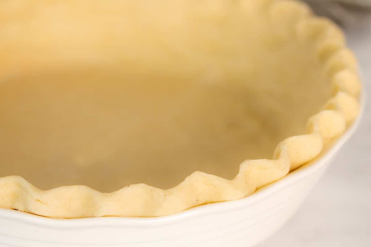 Gluten-free unbaked pie crust with crimped edges in a white dish, perfect for your Thanksgiving recipes.