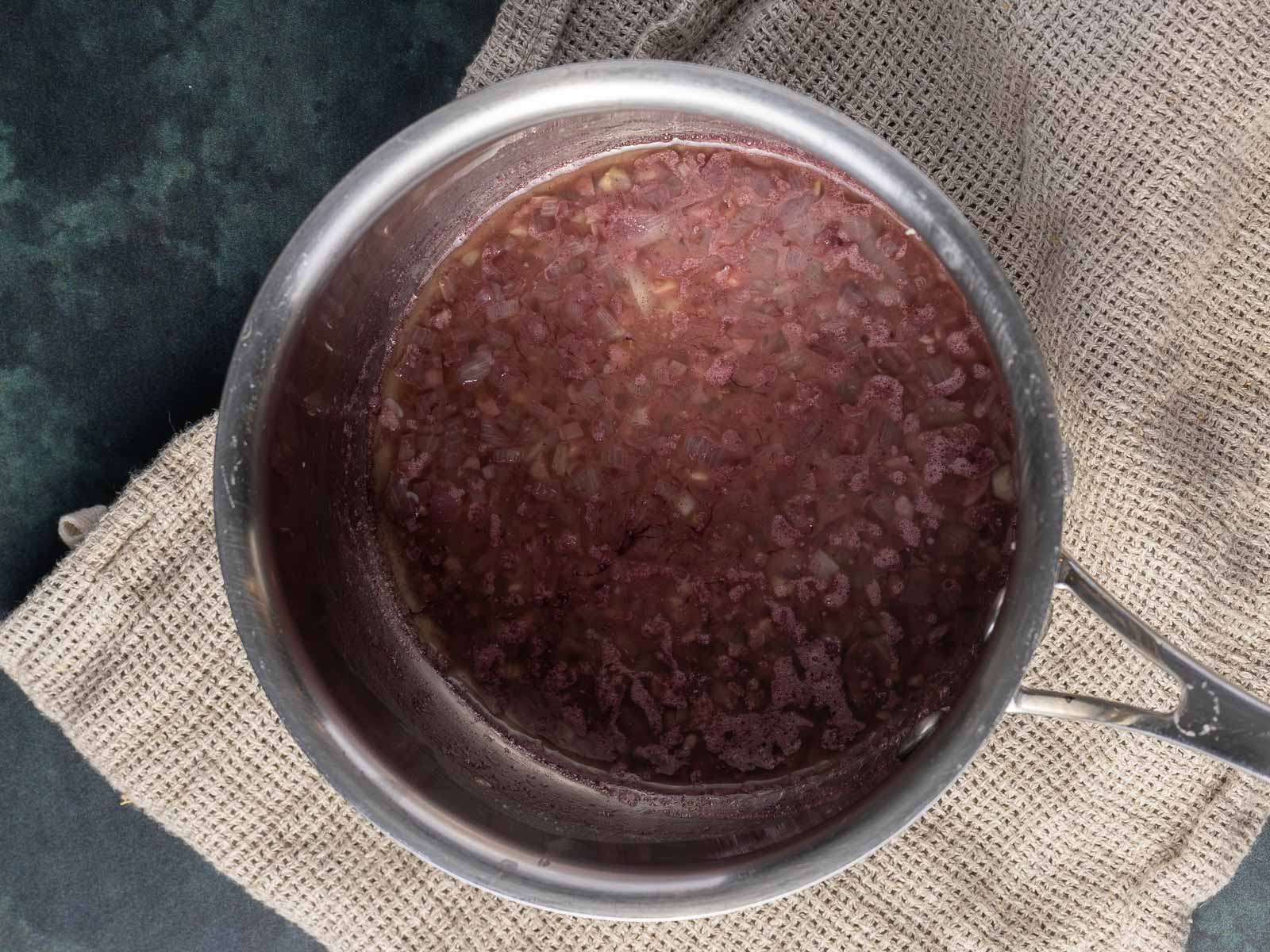 A pot of cooked red onions in rich Au Jus Sauce rests on a textured cloth, viewed from above.