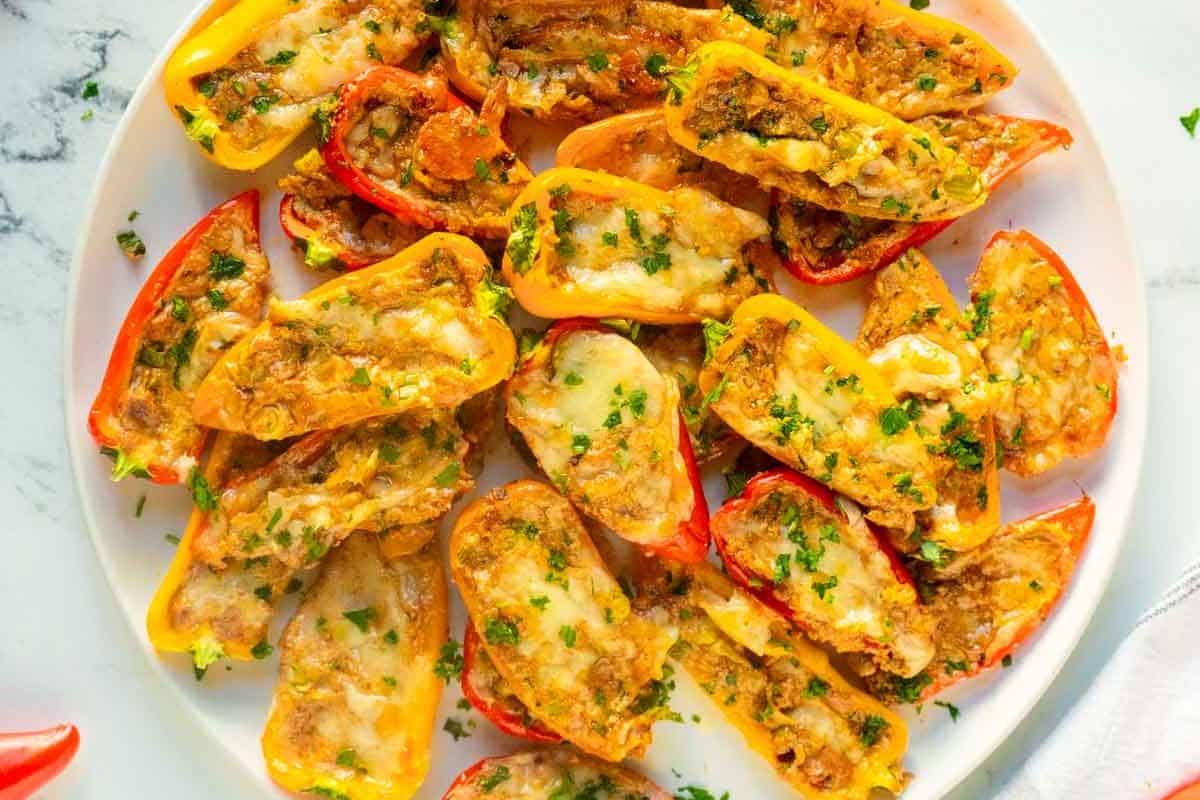 A plate of halved mini bell peppers filled with a cheese and herb mixture, garnished with chopped parsley.
