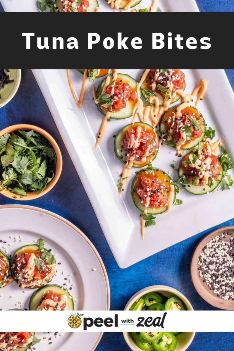 Plates of tuna poke bites topped with sesame seeds and sauce, surrounded by bowls of herbs, sliced jalapeños, and other ingredients on a blue surface.