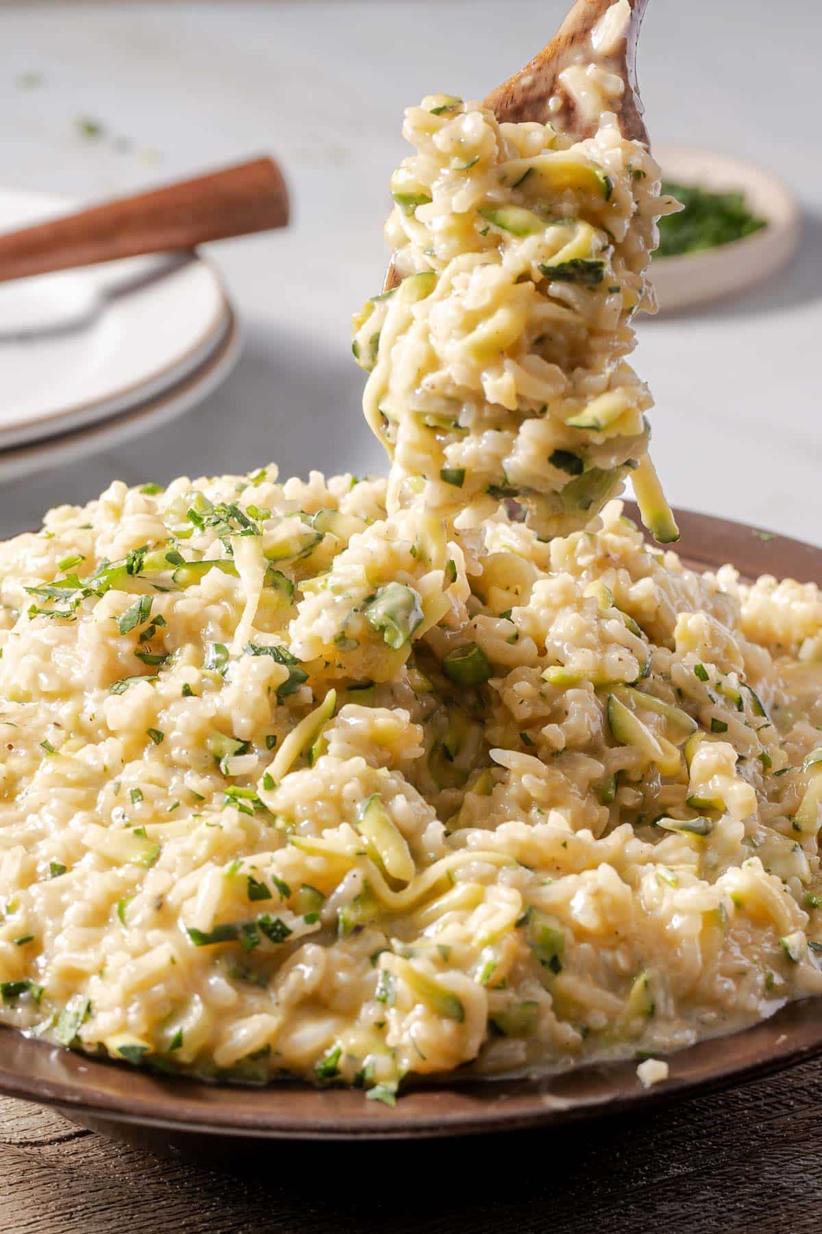 A spoon lifts a portion of creamy zucchini risotto from a bowl, with visible parsley garnish.
