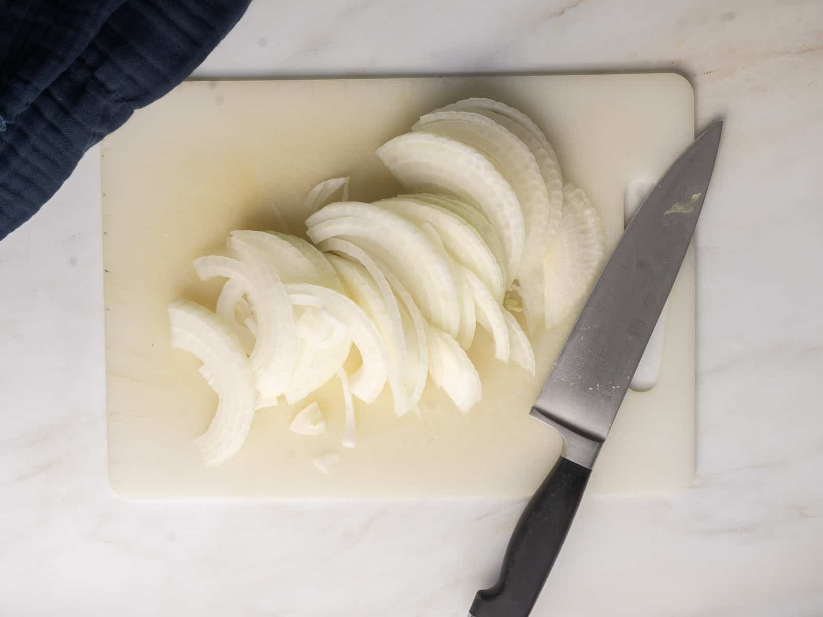 Sliced onions on a white cutting board next to a knife.
