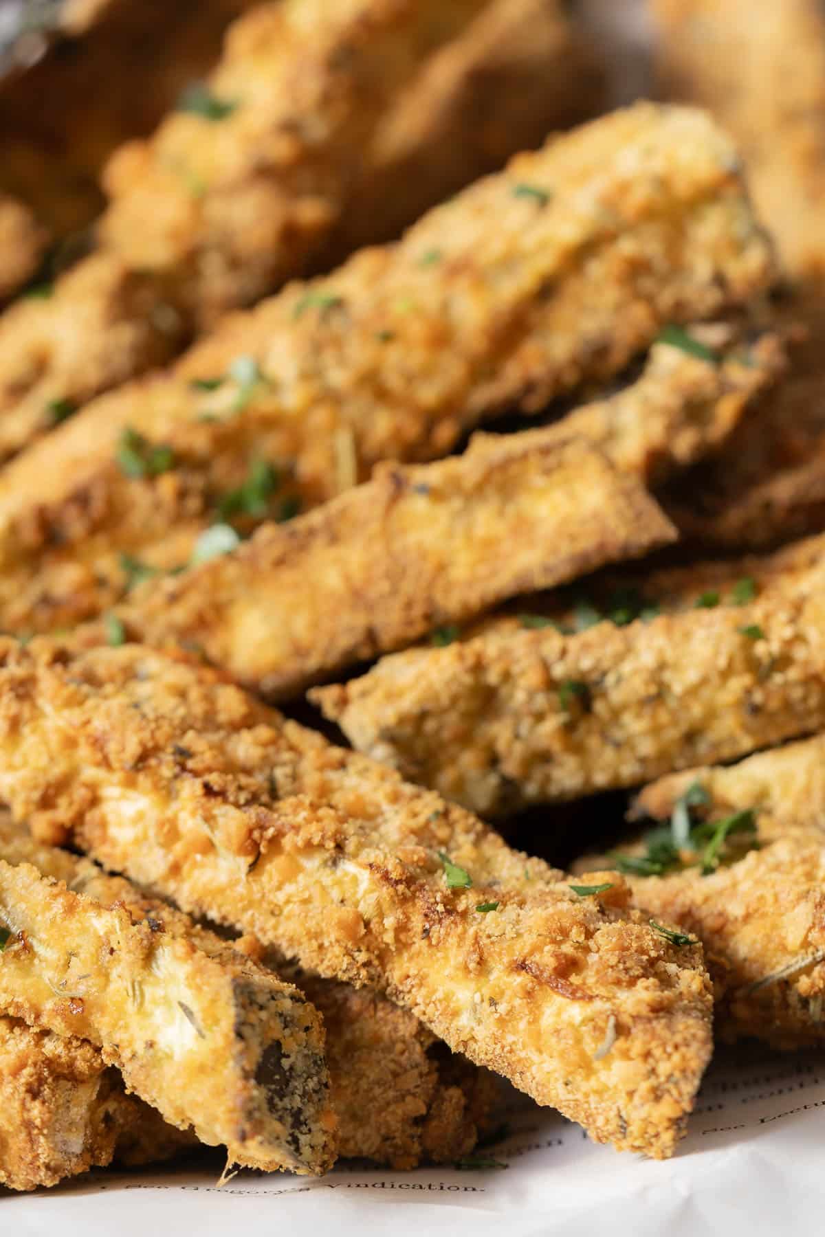 Close-up of crispy breaded zucchini sticks garnished with herbs on a plate.