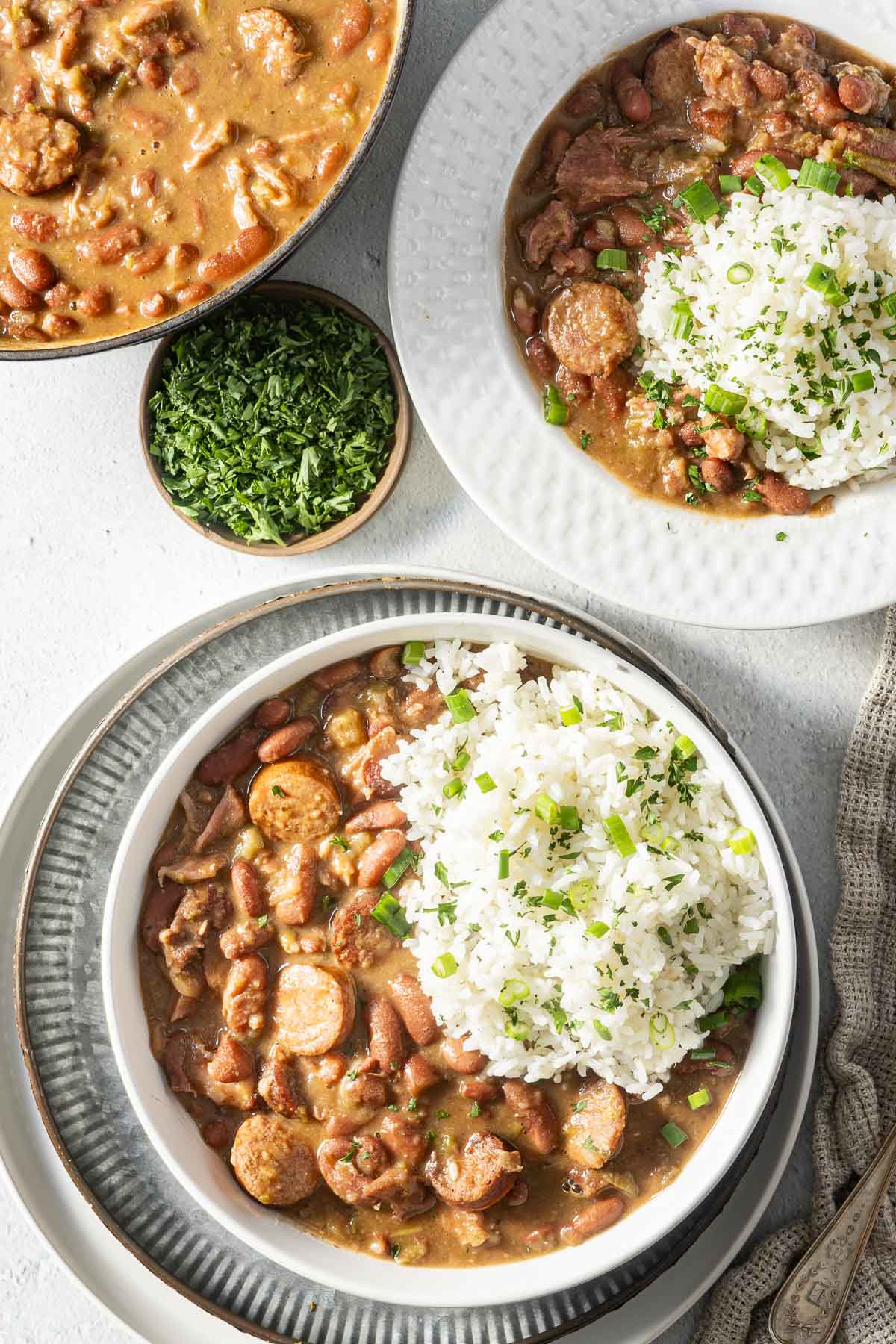 Bowls of red beans and rice topped with herbs are served with a side of chopped parsley.