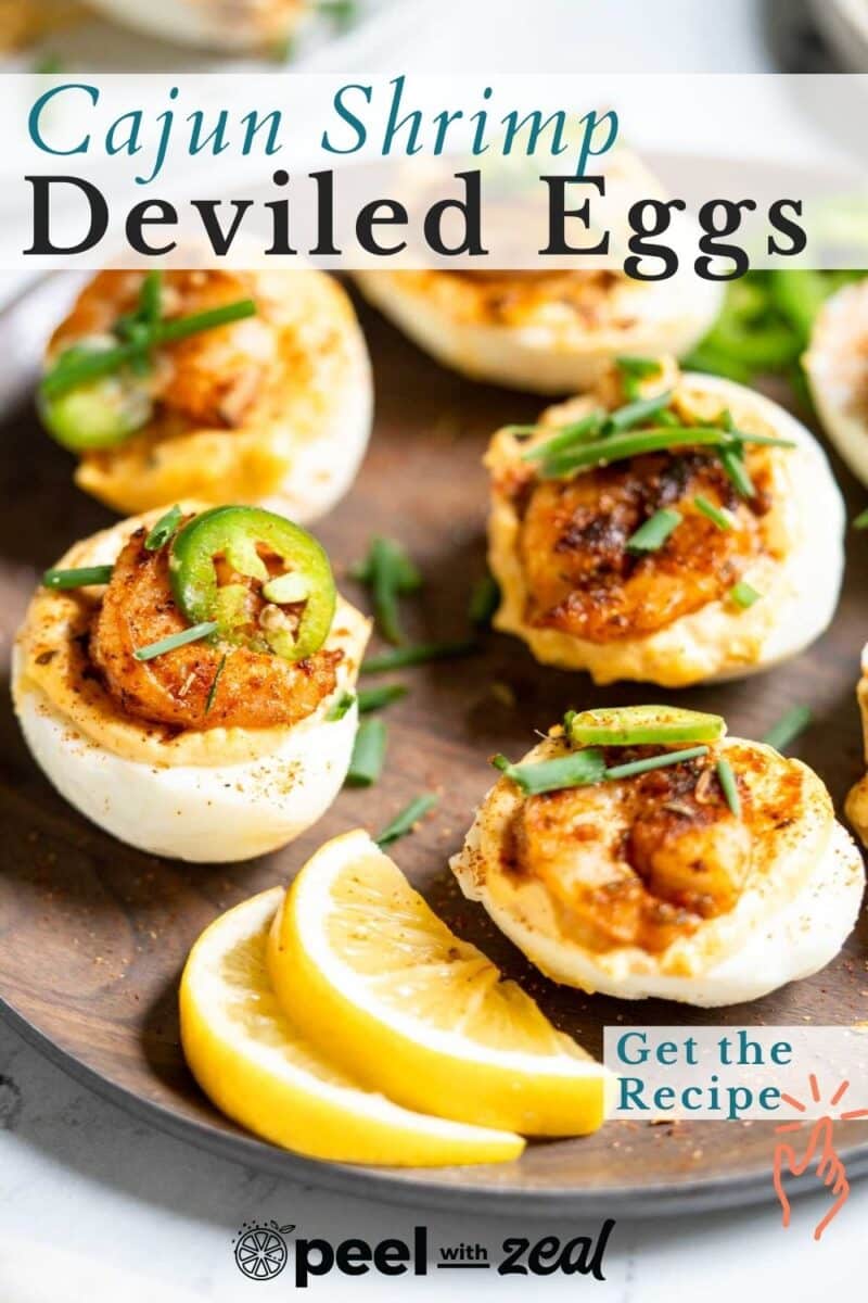 Plate of Cajun shrimp deviled eggs garnished with herbs and jalapeño slices, served with lemon wedges.