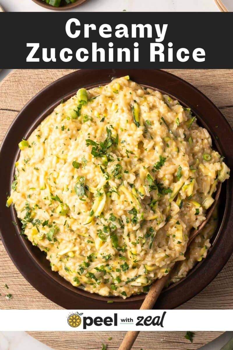 A bowl of creamy zucchini rice garnished with chopped herbs, set on a light wooden table.