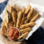 A basket of crispy zucchini fries with a bowl of red dipping sauce.