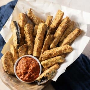 A basket of crispy zucchini fries with a bowl of red dipping sauce.