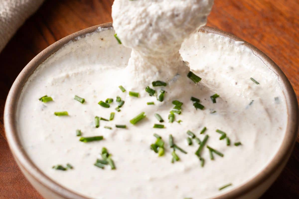 A bowl of creamy dip is garnished with chopped chives on a wooden surface.