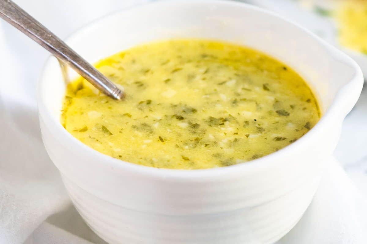 A white bowl filled with creamy yellow sauce with herbs, shown with a spoon.