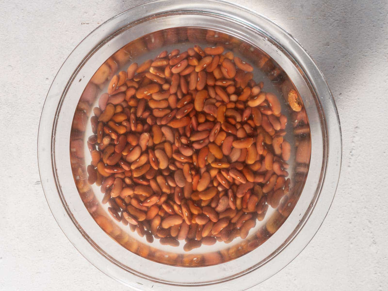 A glass bowl filled with kidney beans soaking in water.