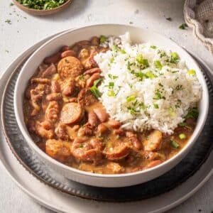 A bowl of red beans and sausage stew with a portion of white rice, garnished with chopped green herbs.