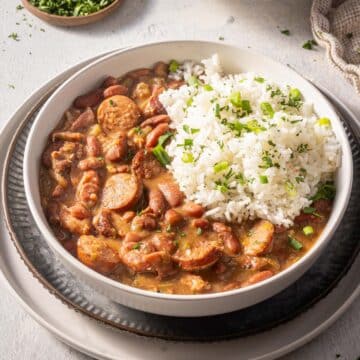 A bowl of red beans and sausage stew with a portion of white rice, garnished with chopped green herbs.