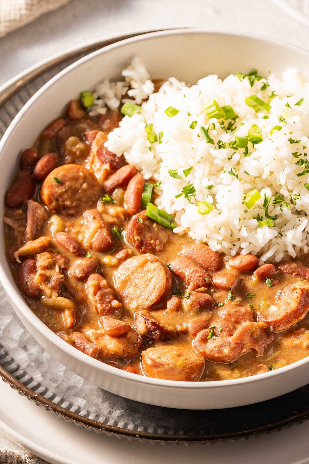 A bowl of Cajun red beans served with white rice, garnished with chopped green herbs.