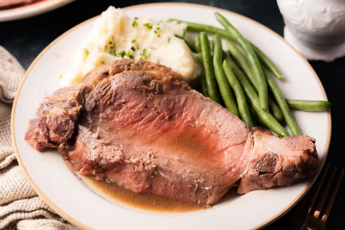 A plate with a slice of roast beef, mashed potatoes with herbs, and green beans.