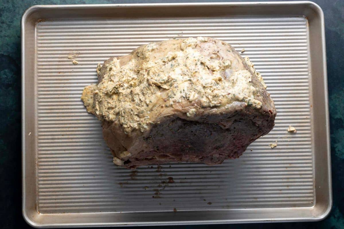 A raw seasoned meat roast on a metal baking sheet.