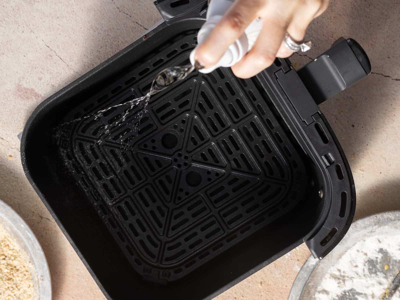 A person pours oil into an empty air fryer basket on a countertop.