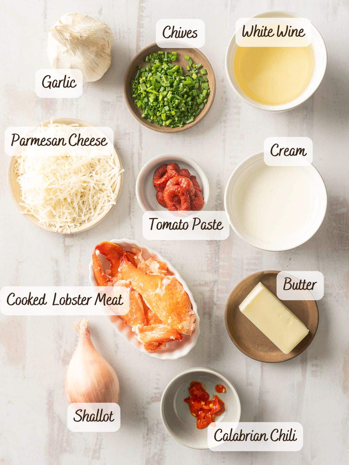 Ingredients for a delectable dish are arranged on the table: garlic, chives, white wine, parmesan cheese, cream, tender lobster meat, butter, shallot, tomato paste, Calabrian chili—all coming together to create the perfect lobster ravioli.