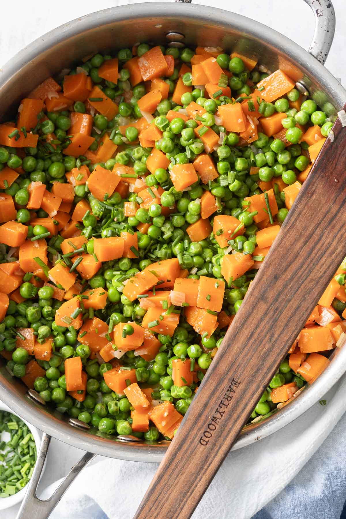 The skillet, boasting a wooden handle, is filled with savory cooked peas and carrots, perfectly mixed with chopped herbs.