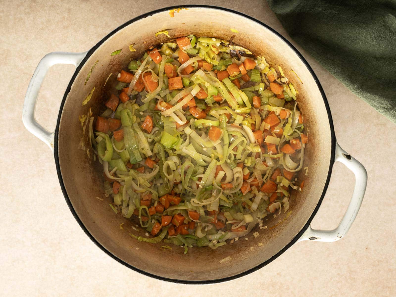 A pot containing chopped carrots, leeks, and onions being sautéed for a flavorful chicken soup.