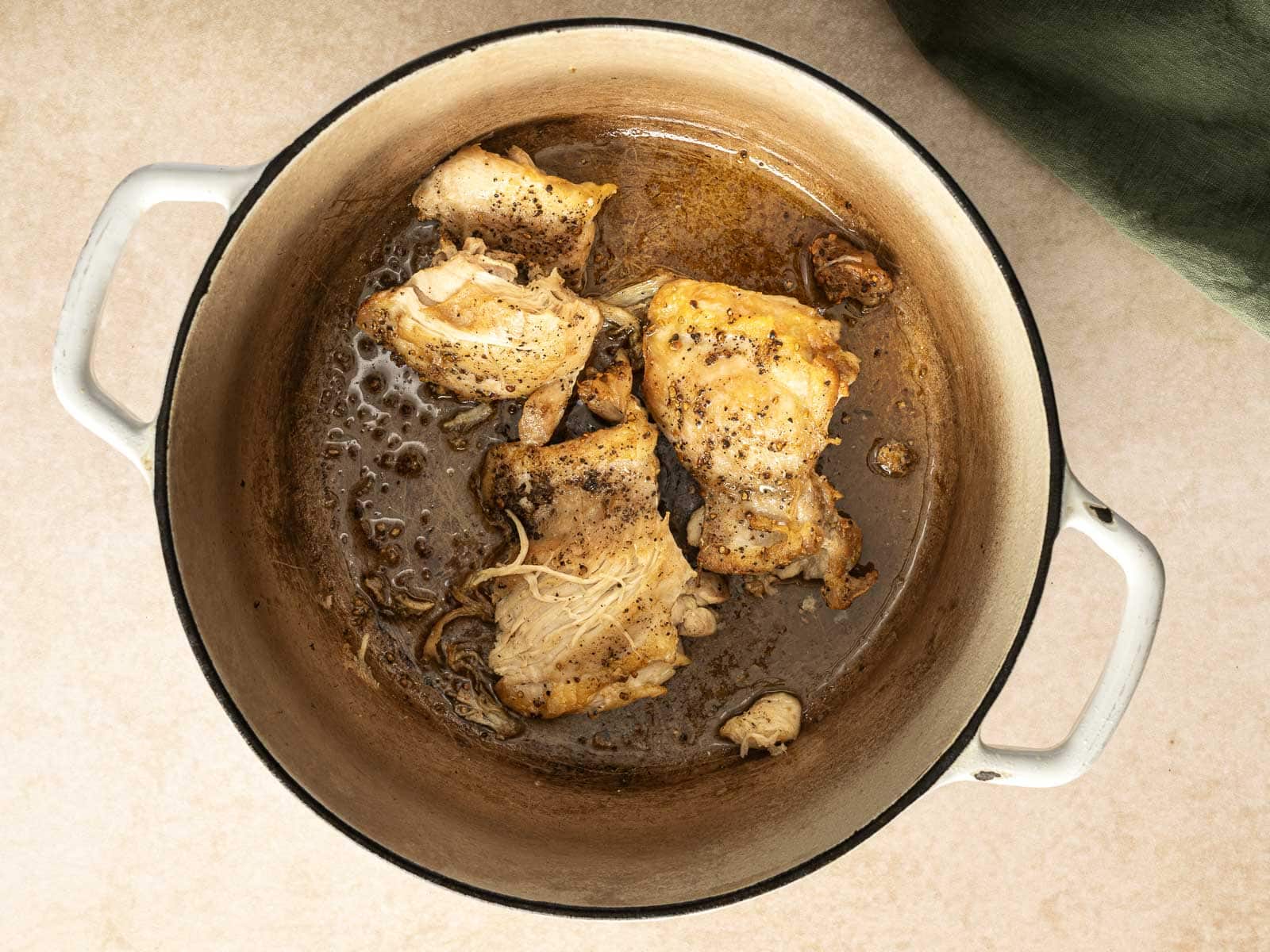 Cooked chicken pieces with seasoning in a round, deep dish on a light surface, reminiscent of a hearty chicken soup.