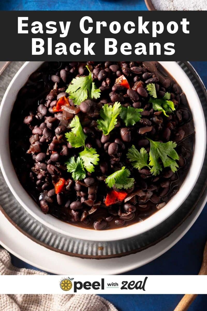 Bowl of black beans garnished with cilantro and red peppers, labeled "Easy Crockpot Black Beans" from Peel with Zeal.