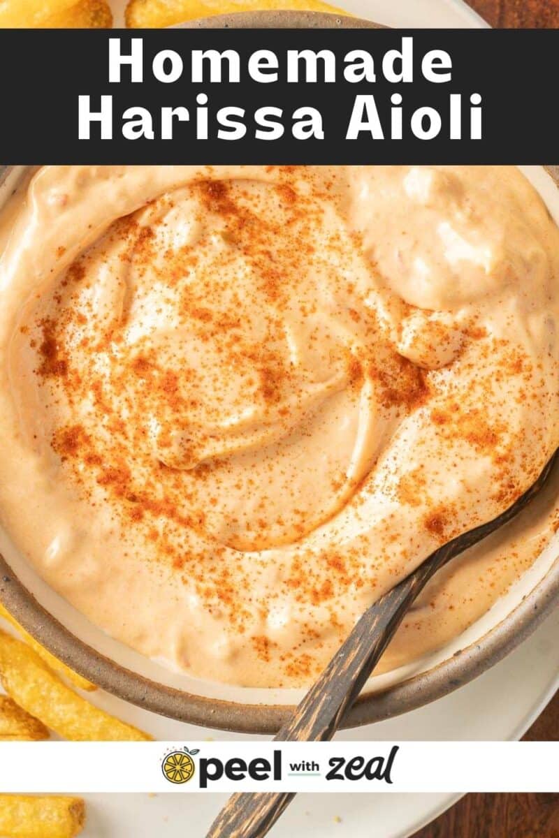 A bowl of homemade harissa aioli with a spoon, garnished with paprika, next to some fries.