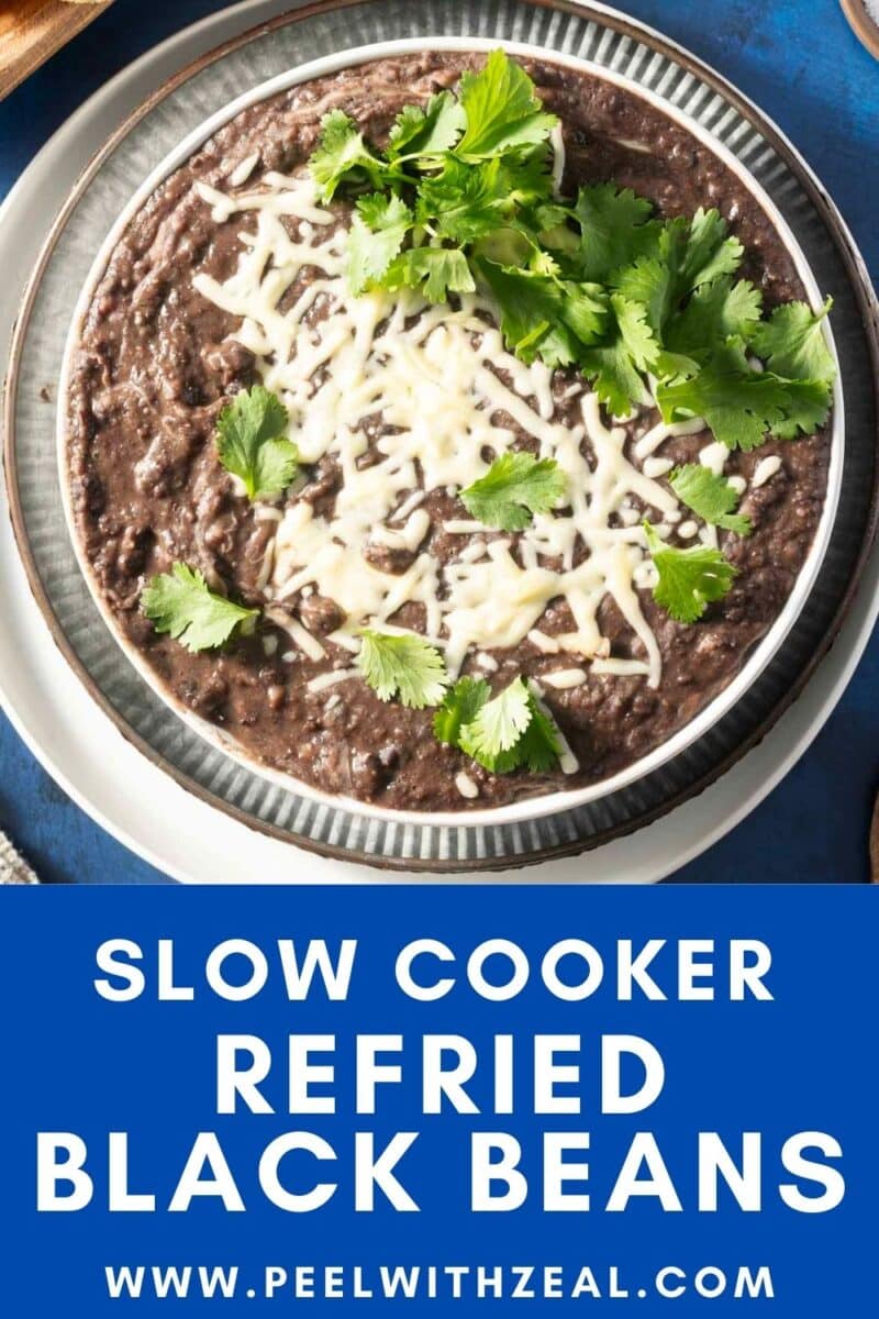 A bowl of refried black beans topped with melted cheese and cilantro. Text at the bottom reads "Slow Cooker Refried Black Beans" with a website link.
