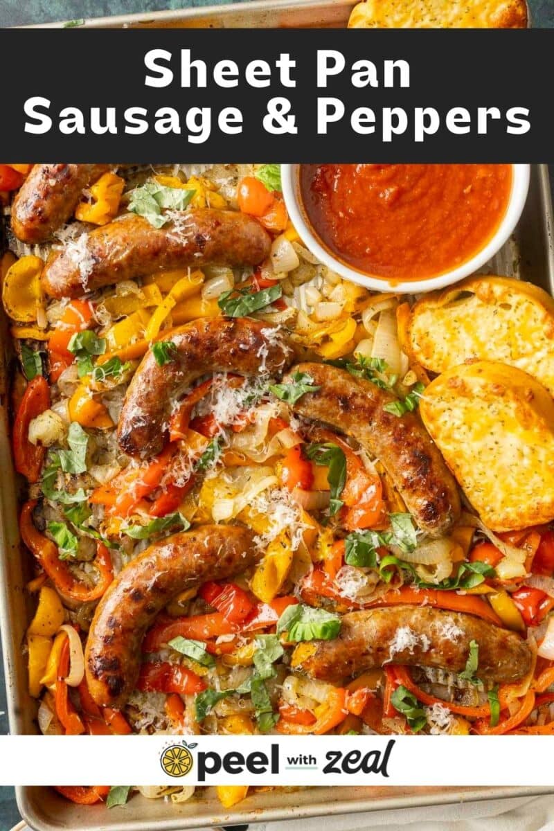 A sheet pan with cooked sausages, sliced red and yellow peppers, onions, herbs, and grated cheese. Two slices of bread and a bowl of tomato sauce are at the corner.
