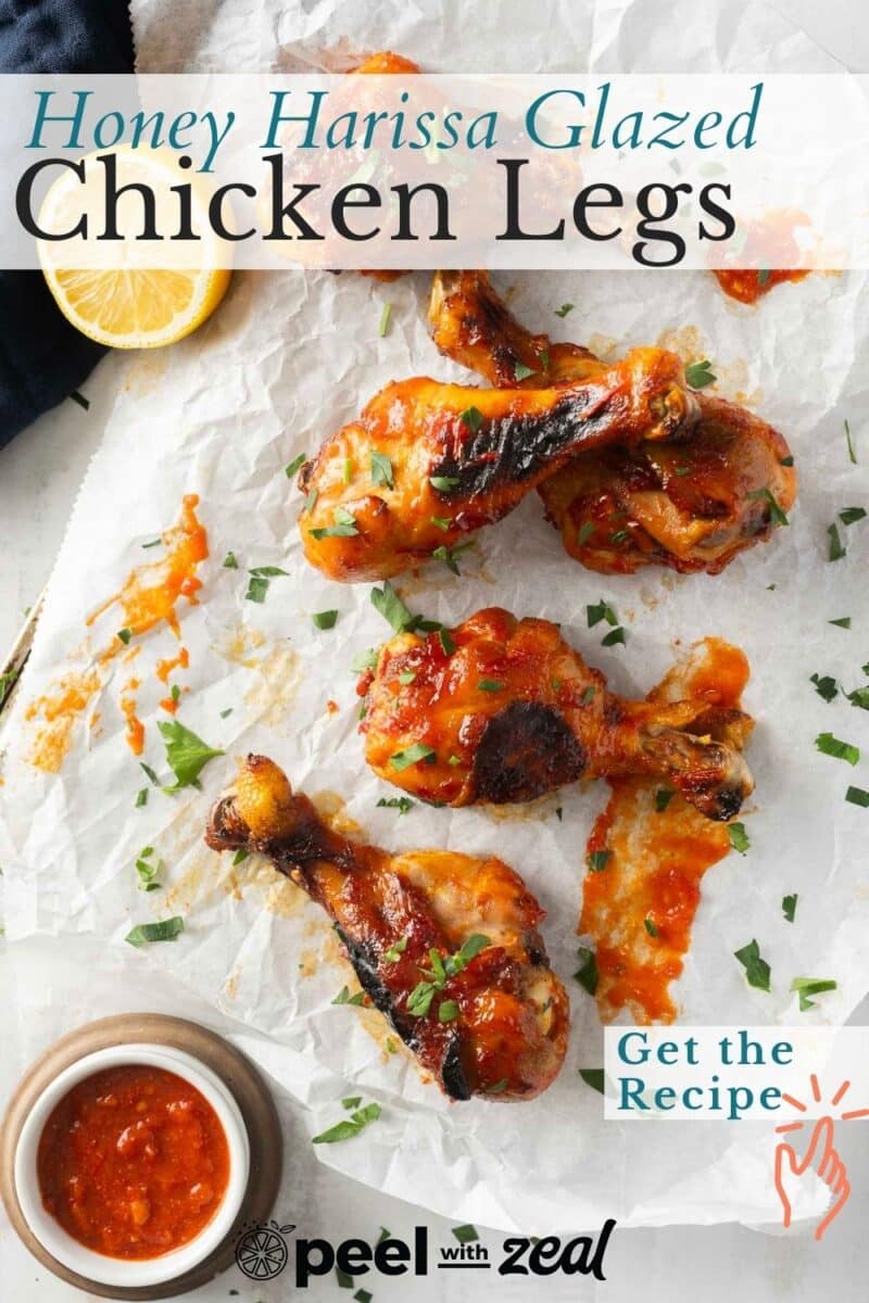 Glazed chicken legs on parchment paper with honey harissa sauce. Lemon slice and small bowl of sauce nearby. Text reads "Honey Harissa Glazed Chicken Legs" and "Get the Recipe.