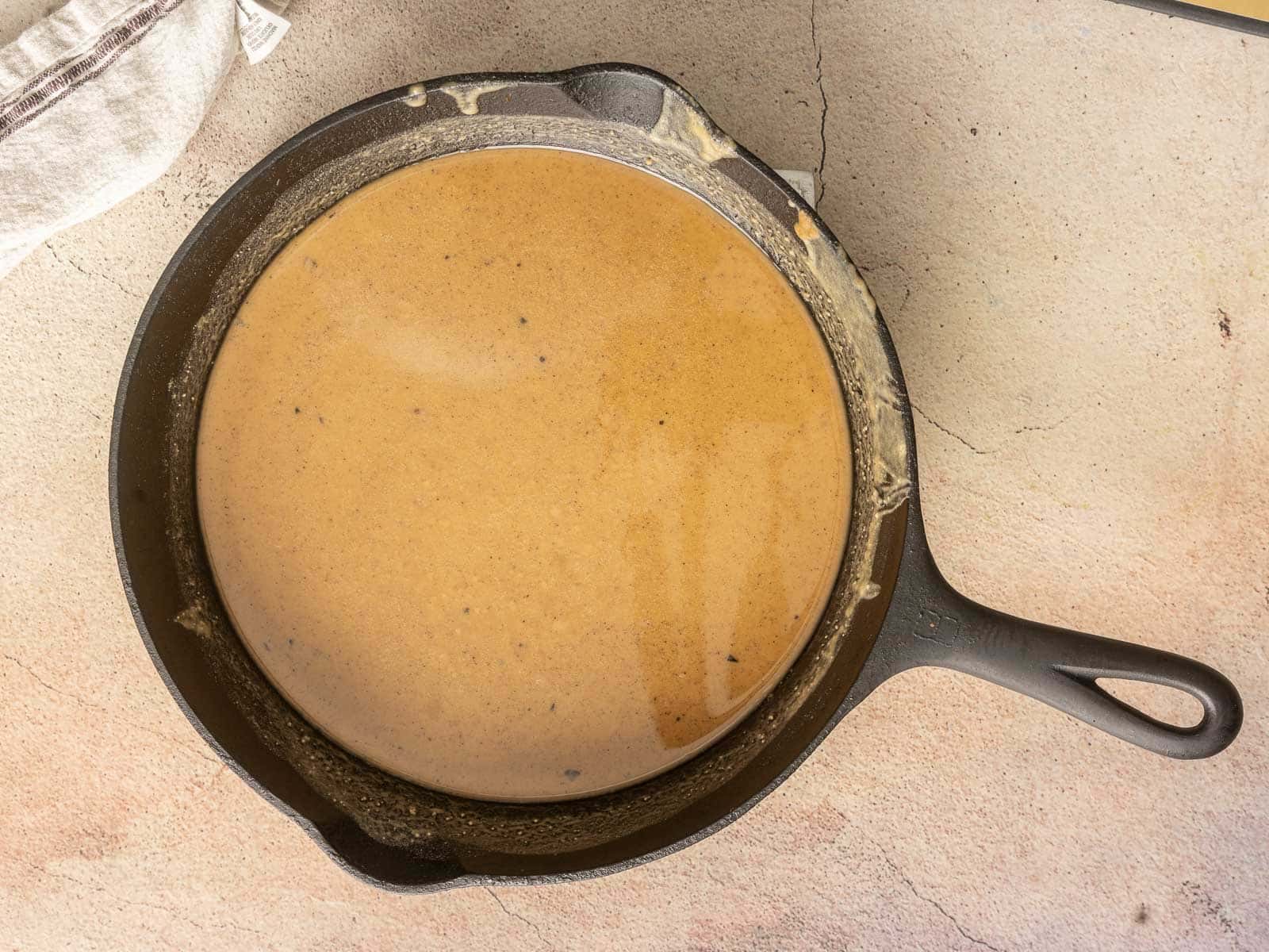 A cast iron skillet brimming with a smooth, brown roux, after 1 hour of baking.