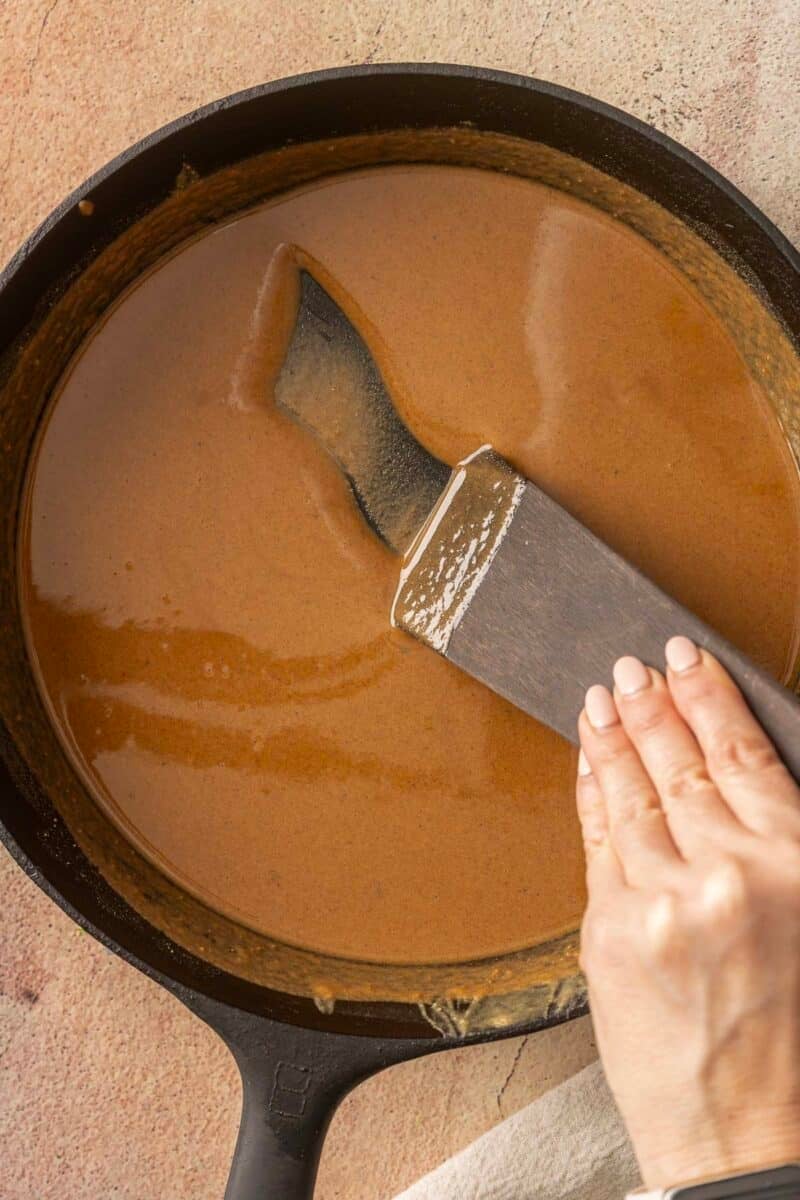 A hand stirs brown roux in a black skillet with a flat spatula, creating a gluten-free roux perfect for an authentic gumbo recipe.