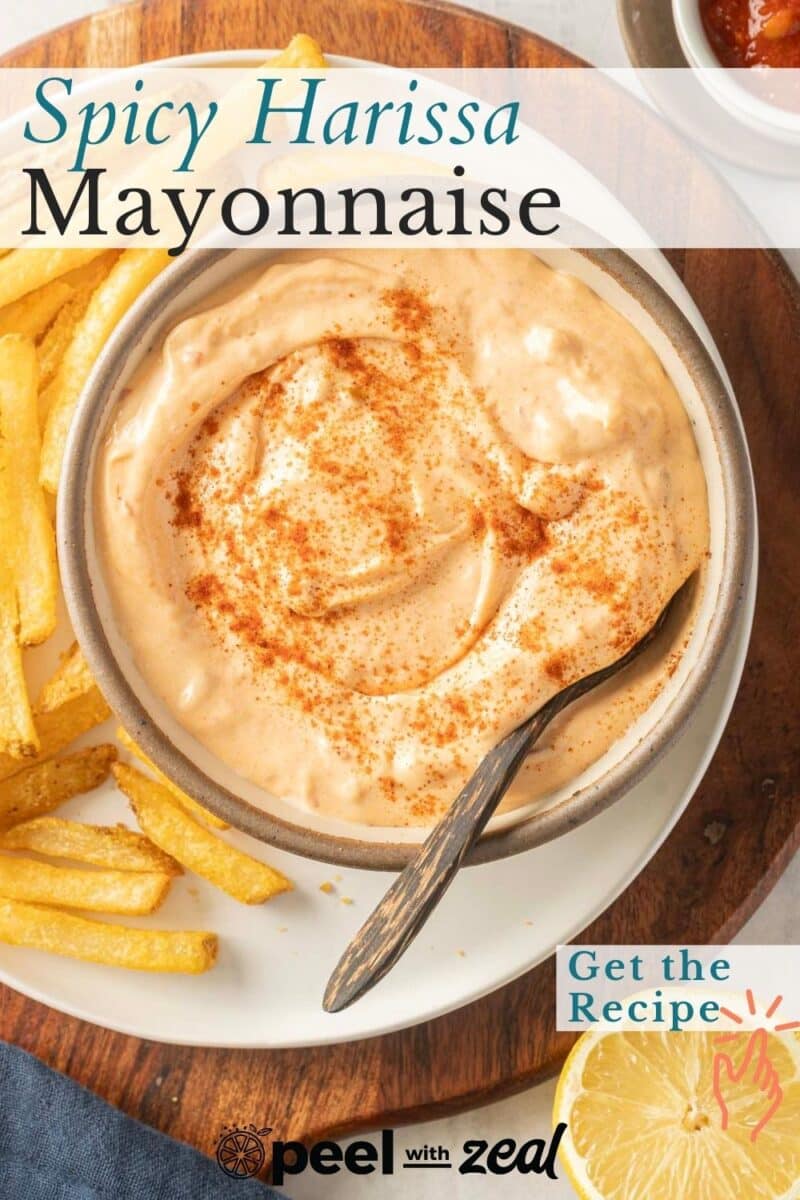 A bowl of spicy harissa mayonnaise with a spoon, surrounded by French fries. Text overlay reads "Spicy Harissa Mayonnaise. Get the Recipe.